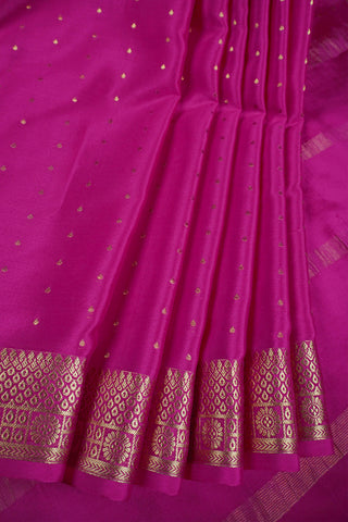 Magenta pink crepe silk saree with scattered gold zari dots and a floral rosette border with lattice bands