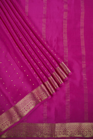 Magenta pink crepe silk saree with scattered gold zari dots and a floral rosette border with lattice bands