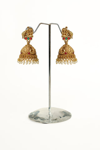 Matt gold temple jhumkas with a Goddess Lakshmi and elephant stud, a peacock-carved dome and white pearl droplets